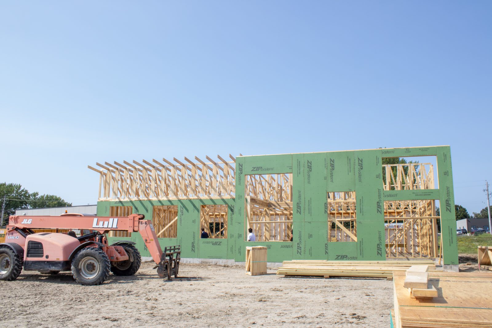 Wide view of the Owatonna clinic construction site with green weather sheathing on the framed walls and a telehandler in the foreground.