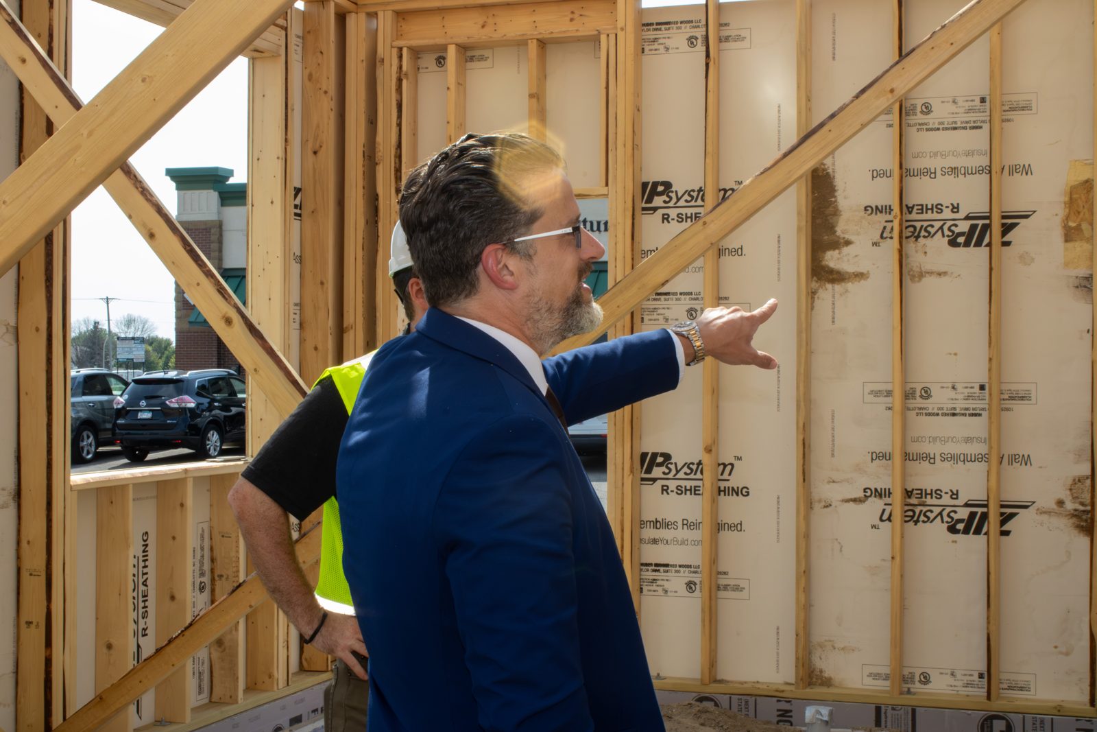 Dr. Christensen in a navy suit and safety vest pointing out features of the framed clinic during a site tour.